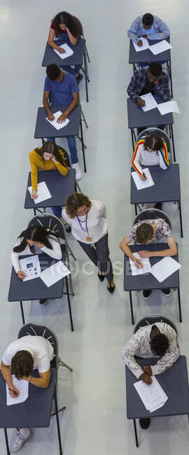 Викладач середньої школи контролює студентів, які складають іспит за столами — стокове фото
