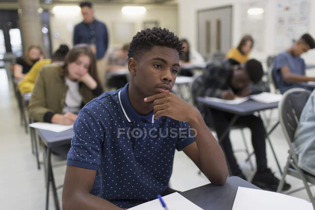 Thoughtful high school boy taking exam at desk in classroom — Stock Photo
