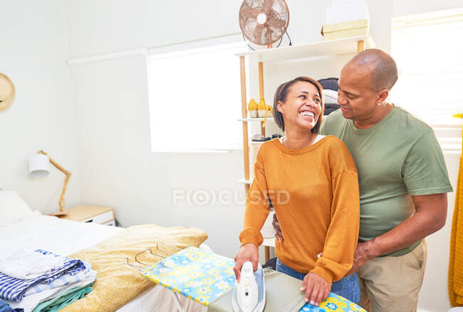 Happy couple ironing and talking in bedroom — Stock Photo