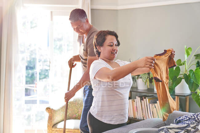 Maduro casal dobrando roupas e varrendo no casa — Fotografia de Stock
