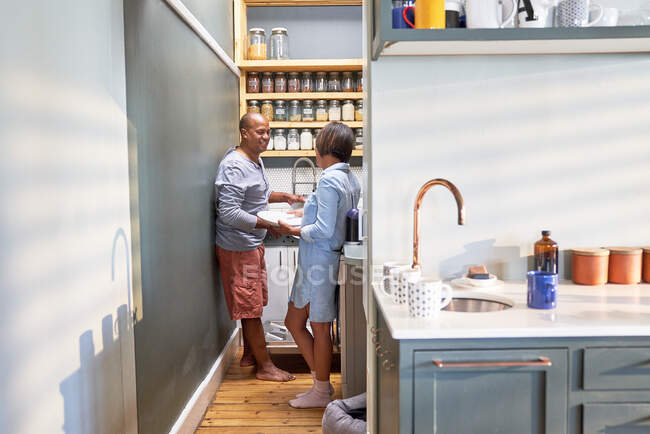 Happy couple talking and doing dishes in kitchen — Stock Photo
