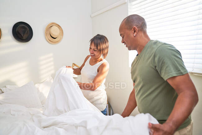 Casal fazendo cama juntos no quarto — Fotografia de Stock