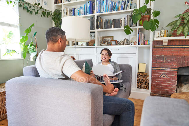 Casal conversando e lendo no sofá da sala de estar — Fotografia de Stock