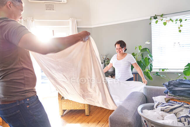 Smiling mature couple folding sheets in sunny living room — Stock Photo