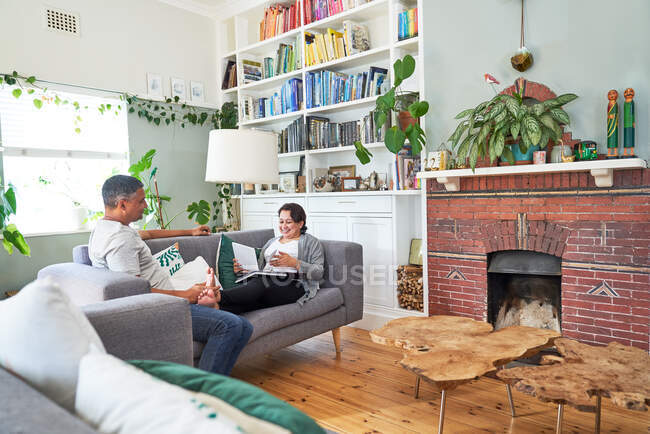 Mature couple reading and talking on living room sofa — Stock Photo