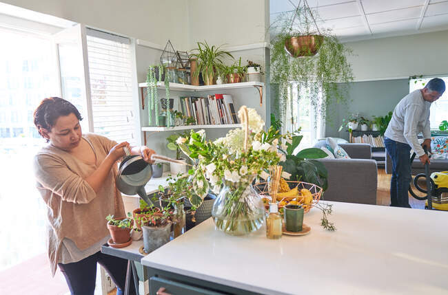 Reife Frau gießt Zimmerpflanzen in der Küche — Stockfoto