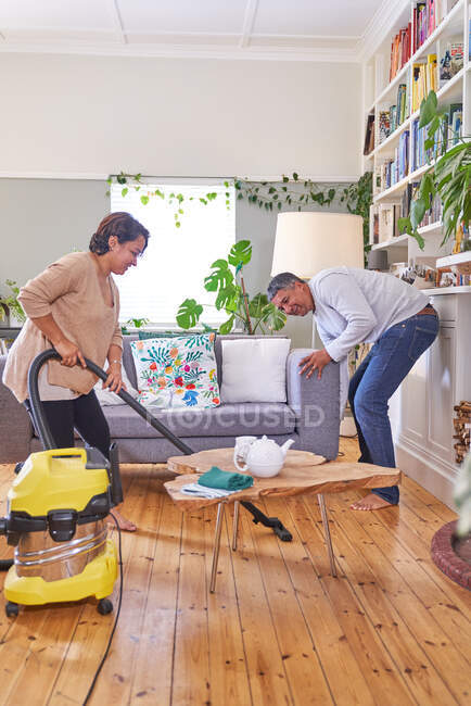 Mature couple vacuuming and cleaning living room — Stock Photo