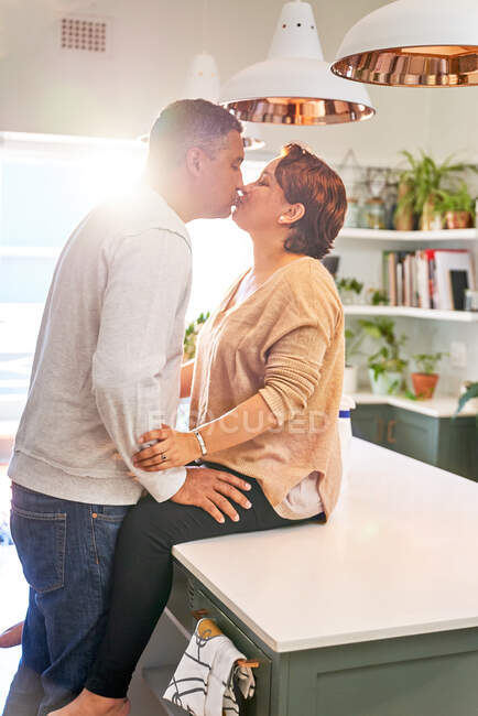 Прихильна зріла пара цілується на кухонному острові — стокове фото
