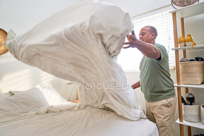 Homem com edredão fazendo cama no quarto — Fotografia de Stock