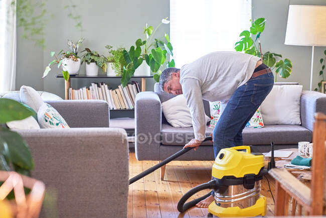 Mature man vacuuming living room — Stock Photo