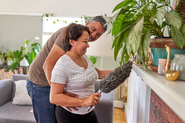 Счастливая любящая зрелая пара вытирает пыль в гостиной — стоковое фото