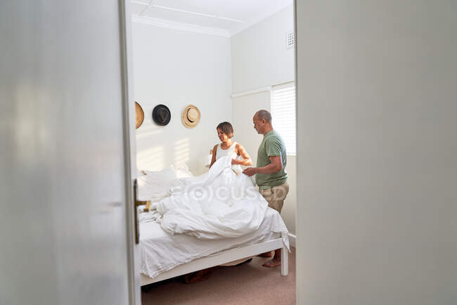 Casal fazendo cama juntos no quarto — Fotografia de Stock