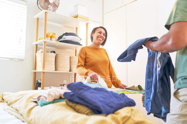 Happy woman ironing laundry and talking with husband - foto de stock
