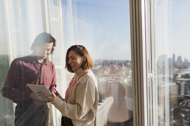 Empresários usando tablet digital na janela do escritório urbano ensolarado — Fotografia de Stock