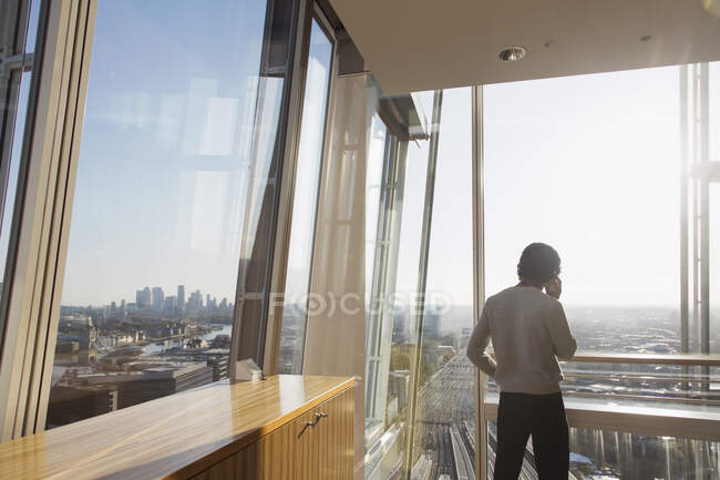 Homme d'affaires parlant sur le téléphone intelligent à la fenêtre moderne ensoleillée highrise — Photo de stock
