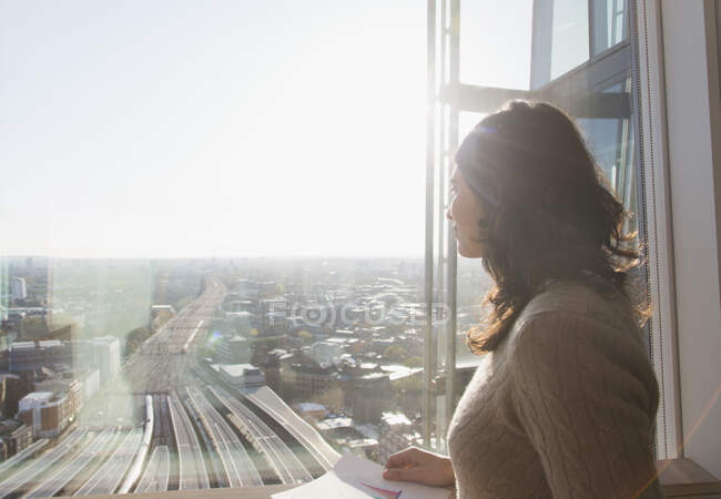 Thoughtful businesswoman at sunny window overlooking city — Stock Photo