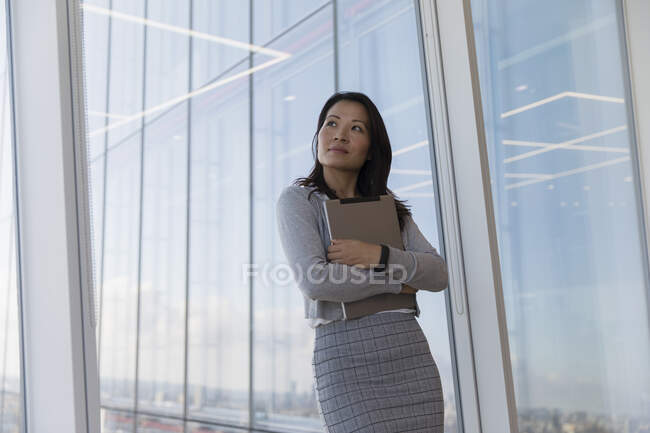 Pensativa empresaria sosteniendo tableta digital en la ventana de rascacielos - foto de stock