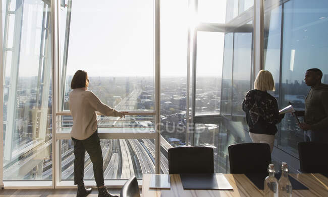 Mujeres de negocios de pie en la ventana soleada de la oficina urbana de rascacielos - foto de stock