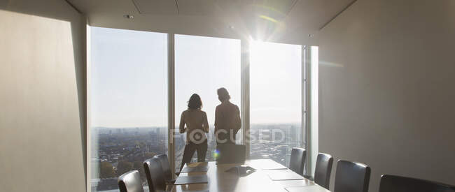 Geschäftsleute stehen am sonnigen Konferenzzimmerfenster eines Hochhauses — Stockfoto