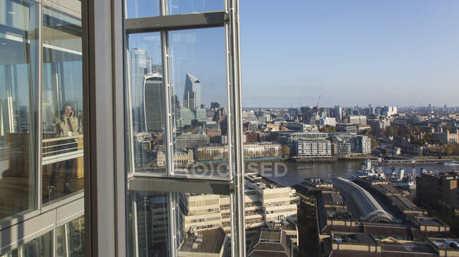 Donna d'affari che utilizza smart phone alla finestra dell'ufficio urbano grattacielo — Foto stock