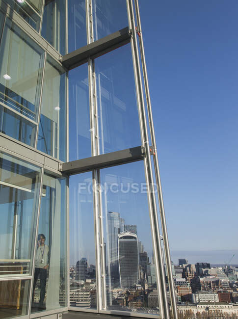 Empresário usando telefone inteligente na ensolarada janela do escritório highrise urbano — Fotografia de Stock