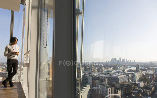 Businessman standing at sunny urban highrise office window — Stock Photo