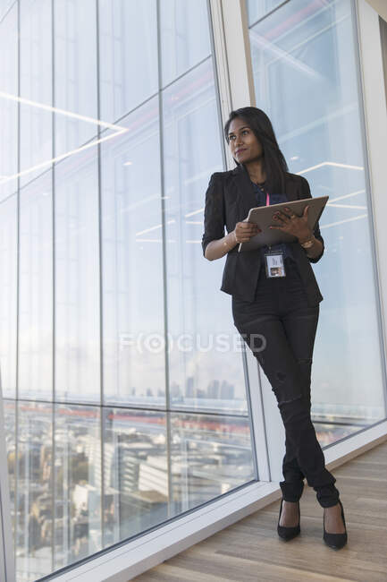 Уверенная деловая женщина с цифровым планшетом у окна высотного офиса — стоковое фото