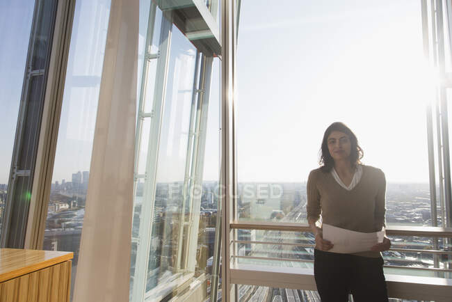 Retrato confiante empresária no ensolarado highrise escritório janela — Fotografia de Stock