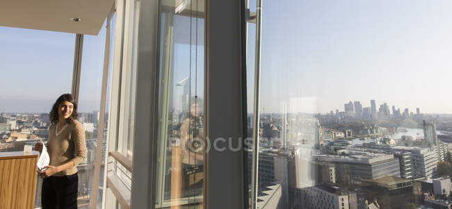 Mujer de negocios sonriente en ventana de oficina de rascacielos urbano soleado - foto de stock