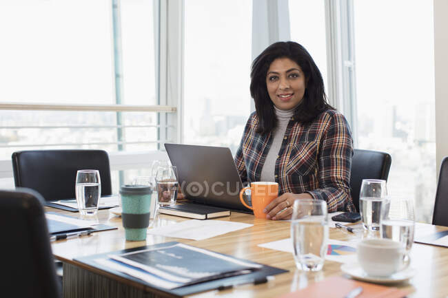 Portrait confident businesswoman using laptop at conference room table — Stock Photo