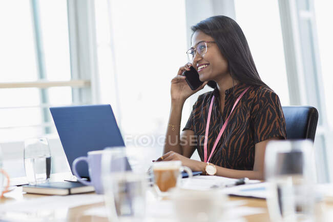 Femme d'affaires souriante parlant sur le téléphone intelligent à l'ordinateur portable — Photo de stock