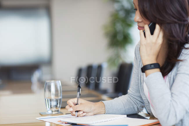 Empresária falando no telefone inteligente e fazendo papelada — Fotografia de Stock