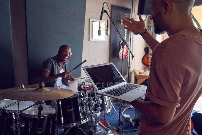 Happy musicians with drums and laptop in recording studio — Stock Photo