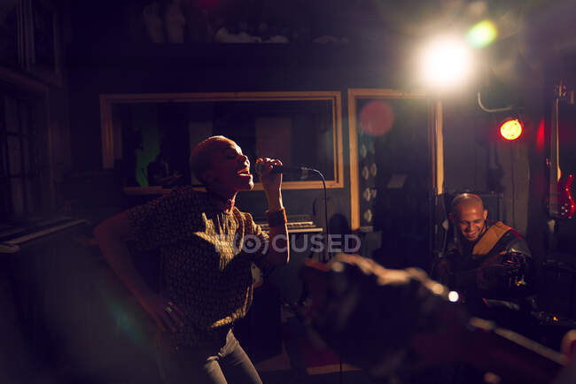 Musicienne chantant dans un micro dans un studio d'enregistrement sombre — Photo de stock