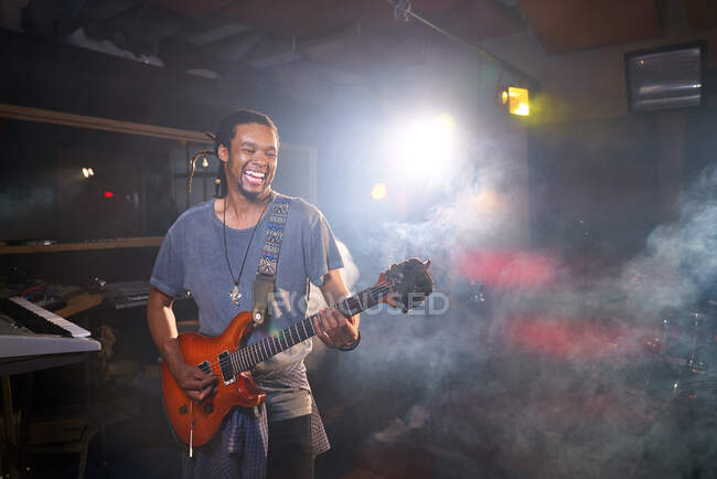 Smiling male musician playing electric guitar in recording studio — Stock Photo