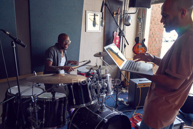 Счастливый мужчина с барабанами и ноутбуком в студии звукозаписи — стоковое фото