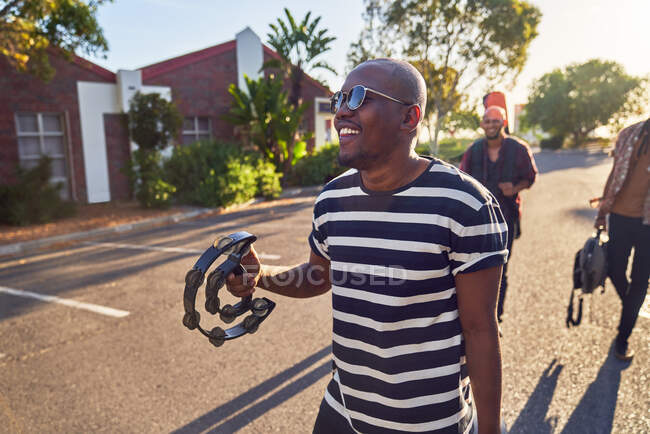 Feliz jovem músico masculino com tambourine na rua ensolarada — Fotografia de Stock