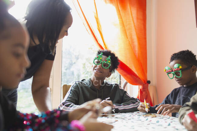Mother and sons in Christmas glasses decorating cookies at table — Stock Photo