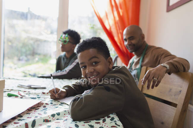 Portrait happy boy writing Christmas cards at table — Stock Photo