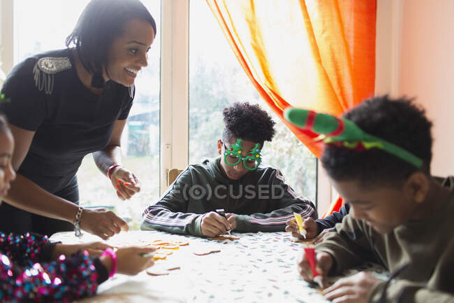 Feliz madre e hijas decorando galletas de Navidad en la mesa - foto de stock