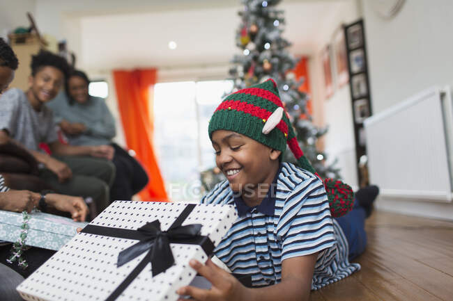 Happy boy opening Christmas gift on living room floor — Stock Photo