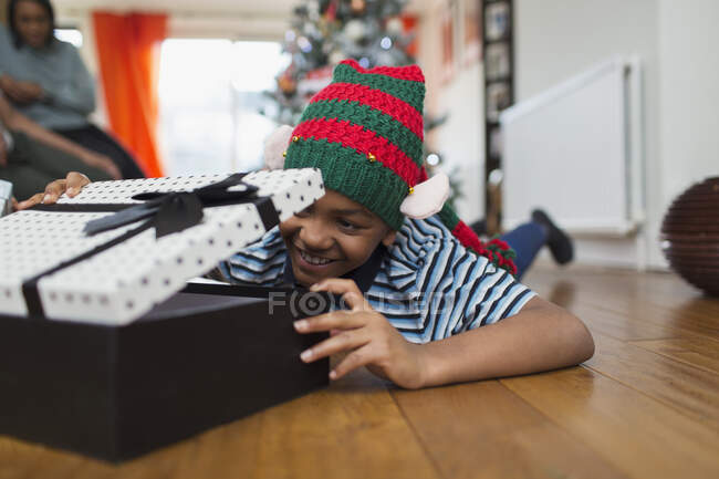 Garoto animado abrindo presente de Natal no chão da sala de estar — Fotografia de Stock