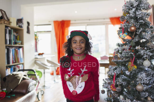 Portrait festive girl in Christmas sweater and hat by tree — Stock Photo