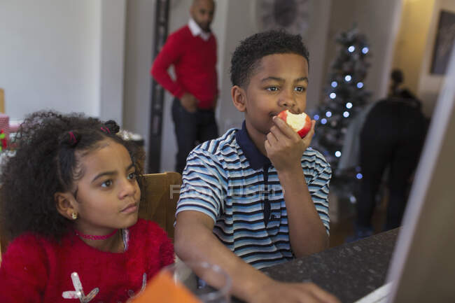 Brother and sister eating apple at computer — Stock Photo