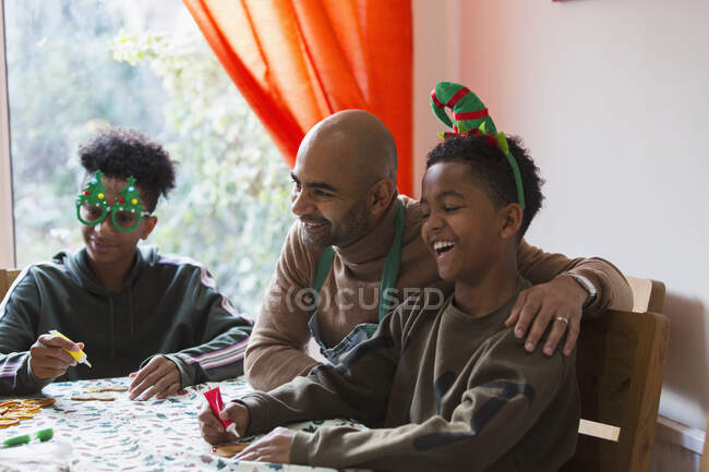 Feliz padre e hijos decorando galletas de Navidad en la mesa - foto de stock