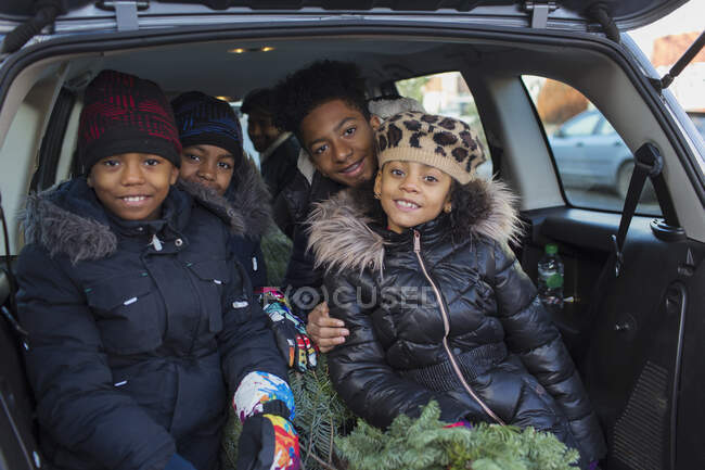Retrato hermanos felices y hermana con árbol de Navidad en la parte trasera del coche - foto de stock