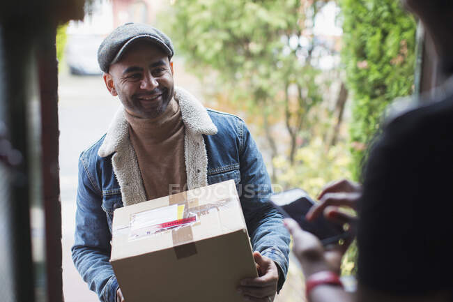 Friendly delivery man with package at front door — Stock Photo