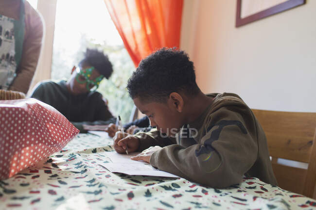 Хлопчик пише різдвяні листівки за столом — стокове фото