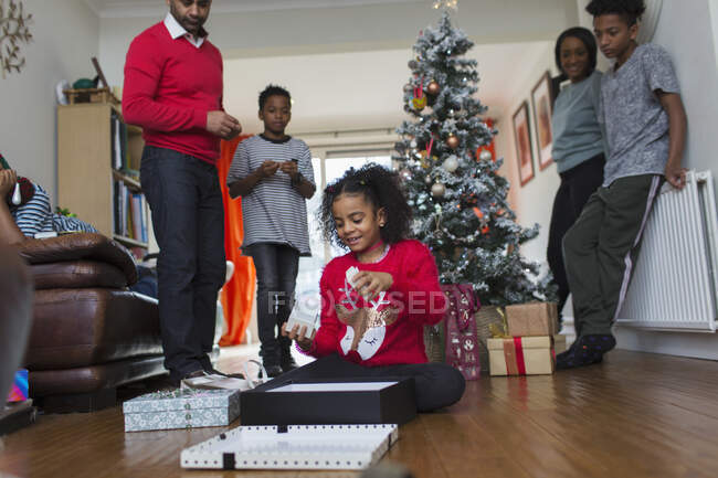 Famiglia guardando ragazza aprire regali di Natale sul pavimento del soggiorno — Foto stock