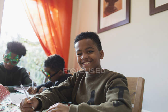 Portrait happy boy writing Christmas cards at table — Stock Photo